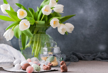Bouquet of white tulips in a vase on a gray background. Shokloy eggs of different colors as a...