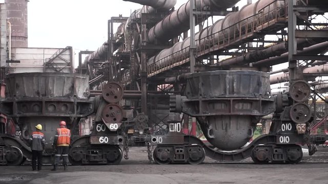 Metal melting vats being transported on big carts to the metal melting shop, heavy industry concept. Stock footage.Two male workers in uniform standing outdoors at the metal smelting plant.
