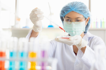Fototapeta premium Female scientist dropping red liquid into beaker..