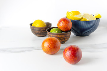 Fresh juicy fruits in the bowls, white marble table.Ripe blood oranges,lime and lemons