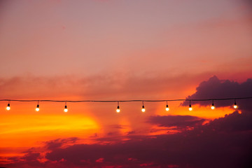 vintage light bulbs on string wire against sunset.