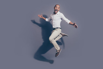 Full length side profile body size photo amazing dark skin he him his macho jumping high great mood childish playful crazy fooling around wear white shirt pastel pants isolated grey background