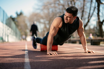 Fototapeta premium Man foam rolling. Athlete stretches using foam roller.