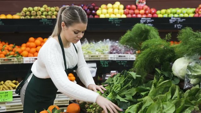 Young female seller in gloves working with greens and letuce on the supermarket