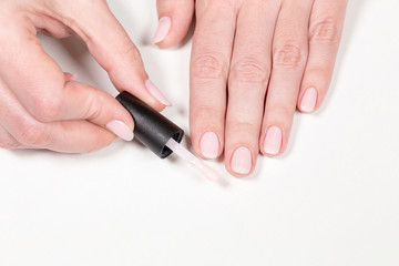 Obraz na płótnie Canvas Closeup top view of brush with pink gel polish and painted manicured female hands isolated on white table background. Horizontal color photography.