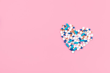 Bright blue and white pills and tablets in heart shape on pink background. Medicines, drugs,...