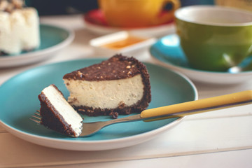 Salted Caramel Cheesecake on blue plate with fork, yellow tea pot and green cup. Delicious chocolate dessert and tea in cafe. Slice of tasty plain cheesecake