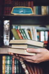 Man, Student holding many books in hands on the background of bookshelves. Male hands hold a large stack of books