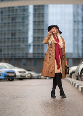 Beautiful young girl on the background of the wet streets of the spring modern city speaks on the phone