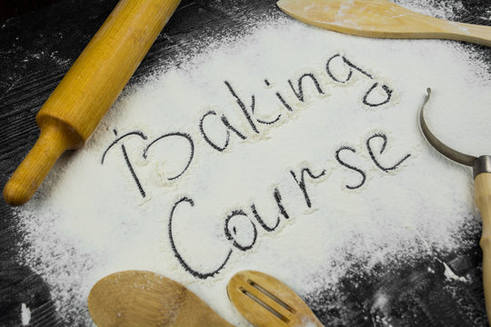 An inscription Baking Course on a black wooden board with kitchen tools