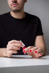 Bearded man holding red nail polish in his hands. Red painted nails. Lifestyle photo. Lgbt community. Transsexual guy.