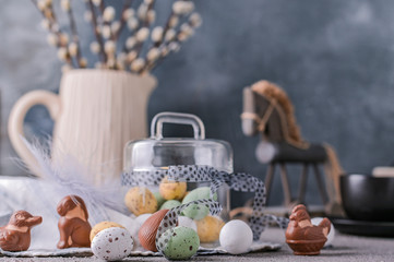 Willow branches in a vase on a gray background and chocolate eggs for the Easter holiday. A bunch of sprout. Card with flowers and sweets. Copy space.