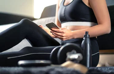 Fotobehang Persoonlijk Online workout course, personal trainer service or fitness app in phone. Fit woman using smartphone while working out at home. Gym, coach or health application on internet. Lady looking at cellphone.  © terovesalainen