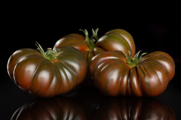 Group of three whole fresh tomato primora isolated on black glass