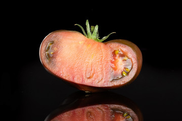 One half of fresh tomato primora isolated on black glass