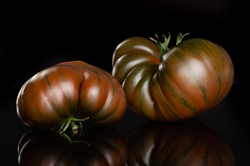 Group of two whole meaty fresh tomato primora isolated on black glass