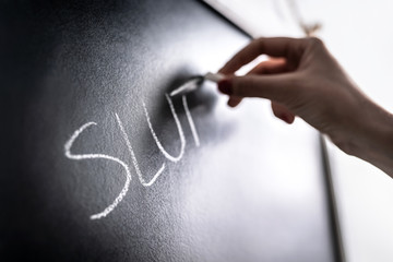 Bullying concept. Mean hate comment and rumour written on chalkboard in school classroom. Sexual...
