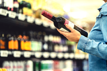 Fototapeta Alcohol shelf in liquor store or supermarket. Woman buying a bottle of red wine and looking at alcoholic drinks in shop. Happy female customer choosing merlot or sangiovese. Shopping spirits concept. obraz