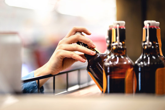 Hand Taking Bottle Of Beer From Shelf In Alcohol And Liquor Store. Customer Buying Cider Or Supermarket Staff Filling And Stocking Shelves. Retail Worker Working. Woman Choosing Lager Or Pale Ale.