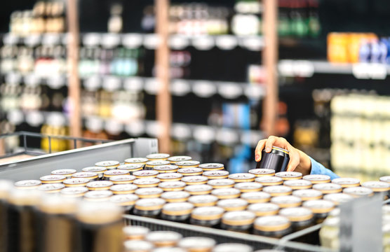 Retail worker filling shelf with drinks in grocery store or customer taking can of beer or soda. Staff at supermarket stocking shelf with alcohol or doing inventory. Woman buying liquor in shop.