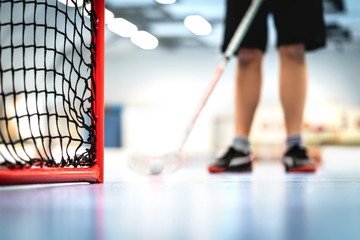 Floorball goal and net. Player training in the background. Man playing floor hockey on court.