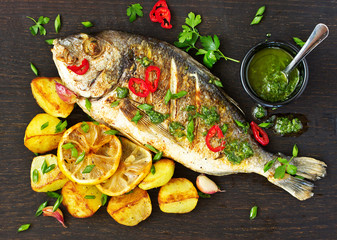 Baked dorado with vegetables and green sauce. View from above.