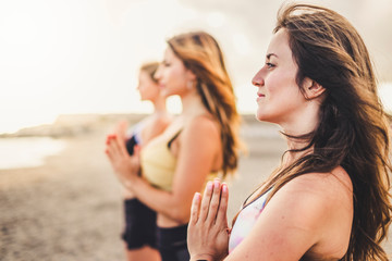 Goup of young women beautiful healthy friends in yoga meditation outdoor at the beach for wellness...