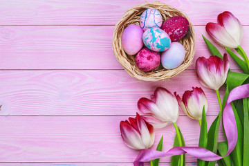 Easter background with colorful eggs and  tulips over pink wood. Top view with copy space