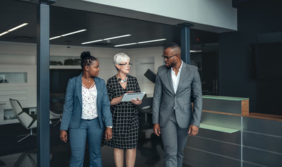 Three corporate business people walking out of a meeting discussing information on an digital tablet looking concerne