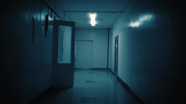 Tracking inside a long dark gloomy corridor, tunnel. On the wall at the end of the path there is a white big clock, it shows a quarter to eleven. Concept of horror.