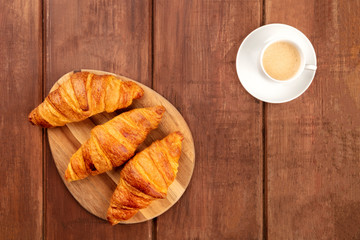 A french breakfast with croissants and coffee, shot from above forming a frame on a dark rustic wooden background with copy space
