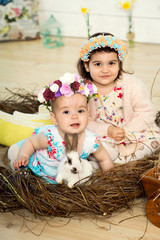 Two little girls sisters in a dress with flowers on their heads are sitting in a nest and shitting...