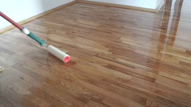 Varnishing lacquering parquet floor by paint roller - second layer. Home renovation parquet. Varnish paint roller strokes on a wooden parquet. Application of a highly glossy parquet lacquer
