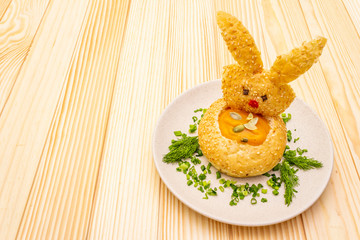 Easter bunny kids food concept. Warm pumpkin cream soup in fresh bun (roll) with herbs and pumpkin seeds in plate. Wooden background, copy space.