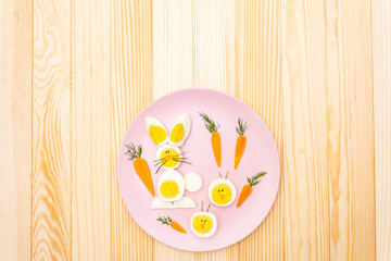 Easter bunny (rabbit) and chicken eggs children (kids) food concept. With carrot on rosy (pink) plate. Wooden background, top view