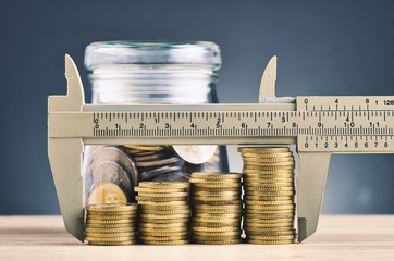 financial crisis and saving money concept, glass jar, Vernier caliper and stacking coins on wooden...