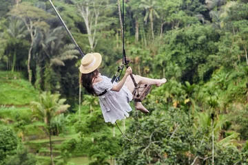 Fototapeten Bali Vacation concept. Happy young woman in white dress and hat swinging at palm grove.  © Dima Anikin