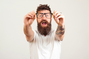 Excited bearded man touching the spectacles and keeping his mouth open against white background....