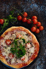 Pizza with ham and rocket on dark ground