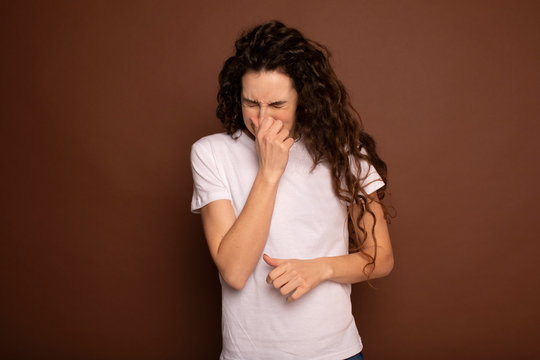 Young Funny Woman Sneezing With Spray And Small Drops, Studio Portrait On Brown Background. Comic, Caricature, Humor. Illness, Infection, Ache. Health Concept 