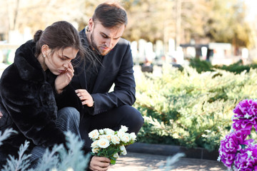 Couple putting flowers on grave of their relative at funeral