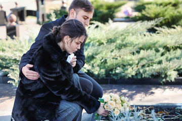 Couple putting flowers on grave of their relative at funeral