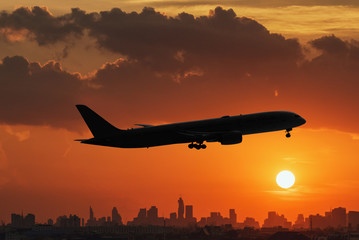silhouette of commercial plane flying over a city during with  sunset in summer