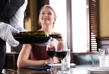 Waiter pouring wine in glasses for clients in restaurant