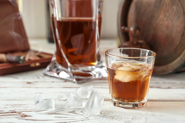 Glass of cold whiskey with ice on white table