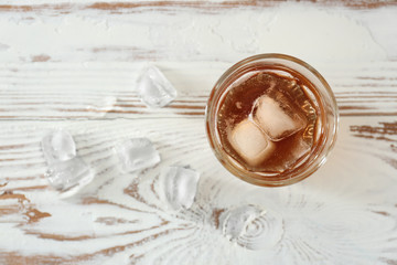 Glass of cold whiskey with ice on white table