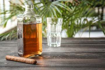 Bottle of cold whiskey with cigar on wooden table