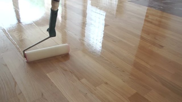 Varnishing lacquering parquet floor by paint roller - second layer. Home renovation parquet. Varnish paint roller strokes on a wooden parquet. Application of a highly glossy parquet lacquer