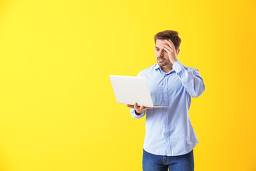 Shocked male programmer with laptop on color background