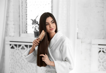 Beautiful young woman brushing her healthy long hair at home